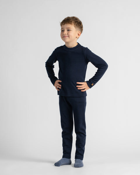 A young boy modeling a dark navy blue long-sleeve top and matching pants set, paired with slate blue socks, standing against a light gray studio background.