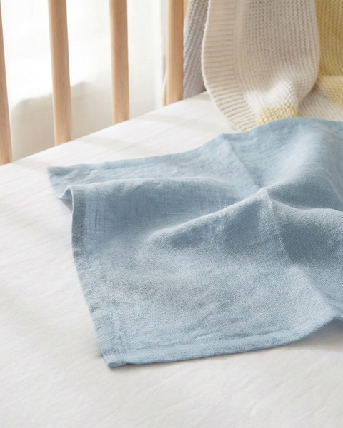 Cloudy blue linen baby burp cloth laid on crib mattress, soft absorbent muslin cloth for newborn feeding and everyday care