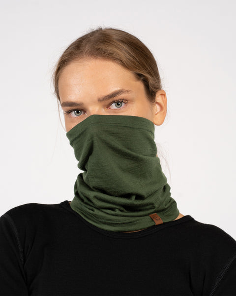 Woman facing forward with a dark green Merino wool neck gaiter covering her nose and mouth, dressed in a black top.