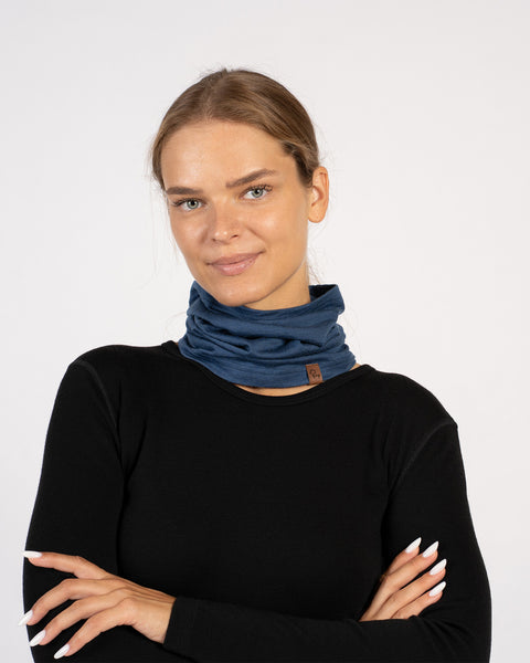 Smiling woman wearing a denim blue Merino wool neck gaiter around her neck as a warmer, paired with a black long-sleeve top.