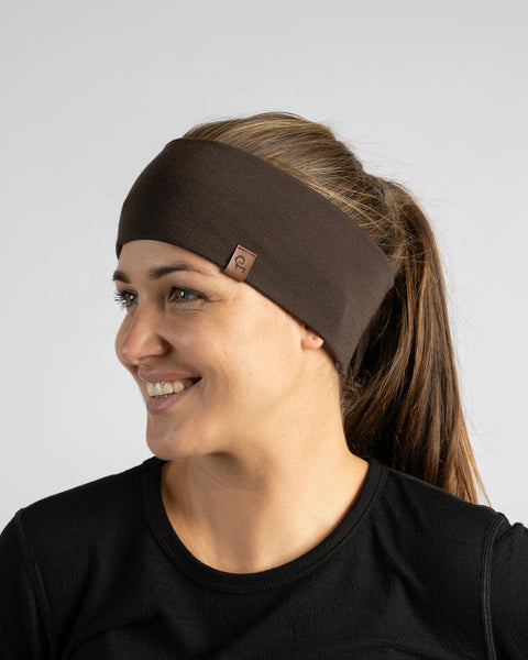 A smiling woman with her hair pulled back into a ponytail, wearing a black top and a wide dark brown knit headband while looking to the side.