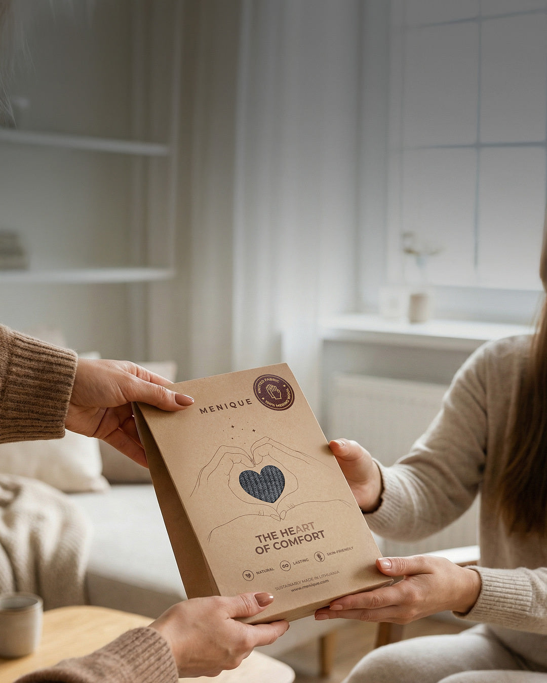 Two people holding a brown package with 'The Heart of Comfort' branding in a kitchen setting.