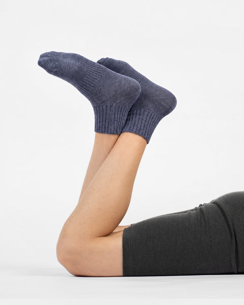 A person lying down with their knees bent and legs raised, wearing dark grey shorts and heathered blue crew socks against a plain white background.
