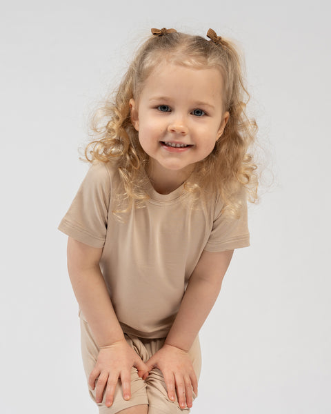 Kids beige bamboo clothing set – girl squatting in soft breathable t-shirt and shorts