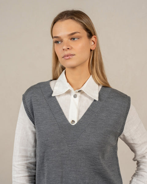 The menique merino wool vest ISLA in gray color. The model is looking to the side, the vest has a v-neck and a relaxed silhouette.