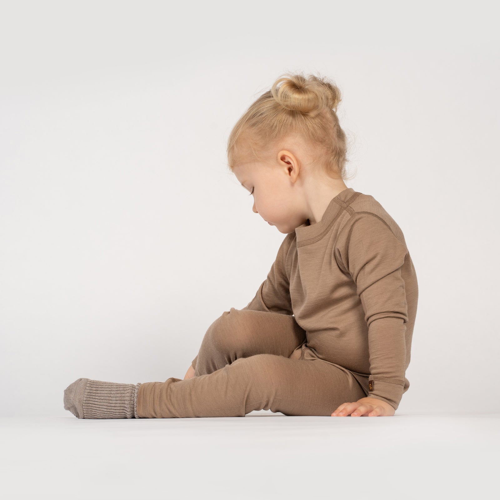 A close-up shot focuses on a child's legs and torso, standing on rocky terrain with a canyon in the background. The child is wearing a dark green long-sleeve top, beige leggings, and gray hiking boots.