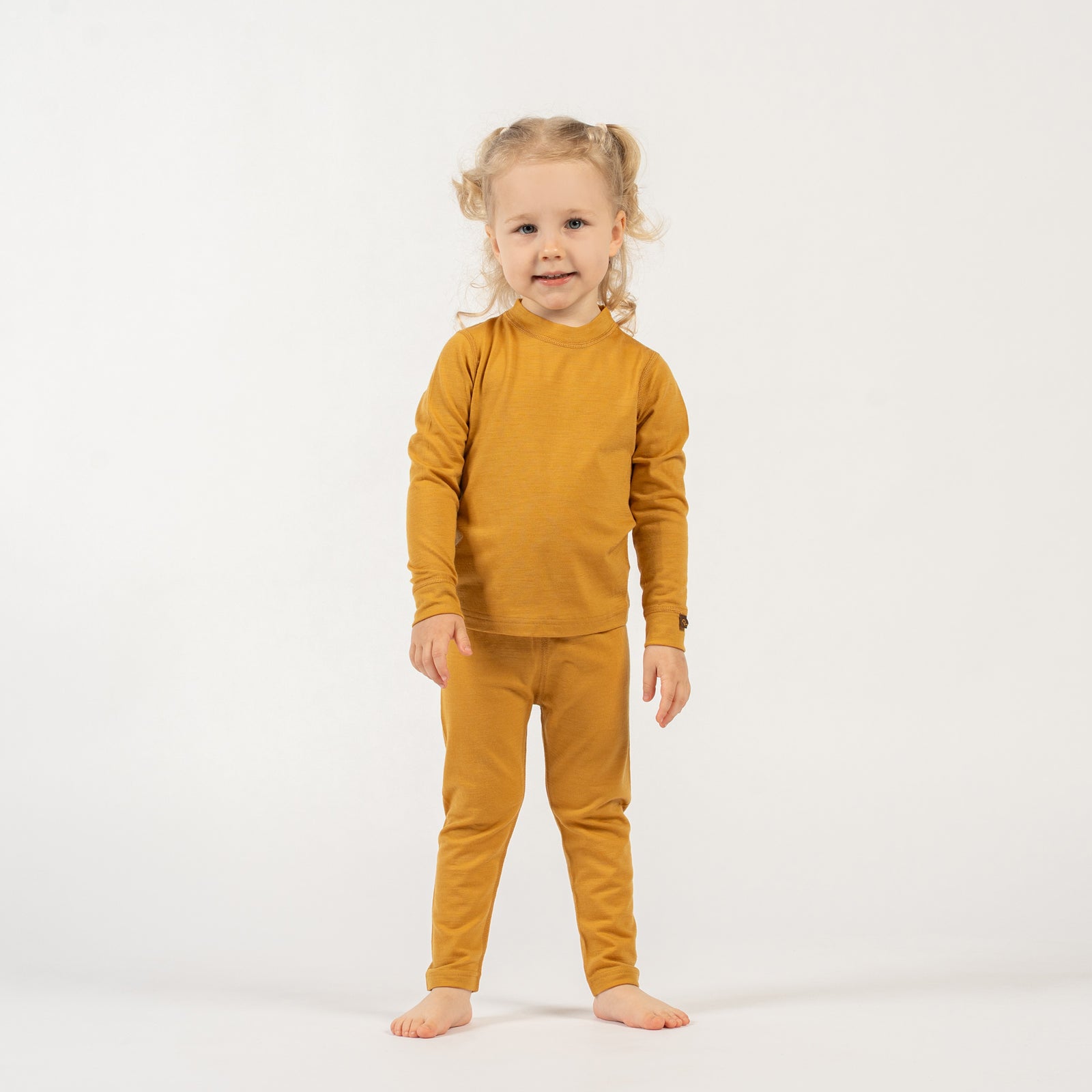 Young girl wearing a menique merino wool yellow long sleeve and bottom set on a white background