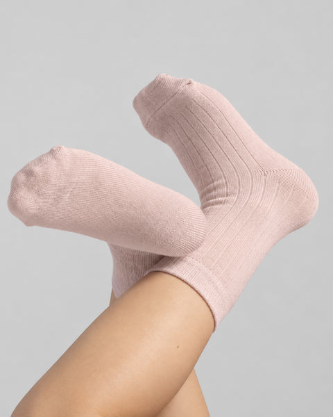 Close-up of bare legs raised upward with feet crossed, wearing soft pastel pink crew socks.