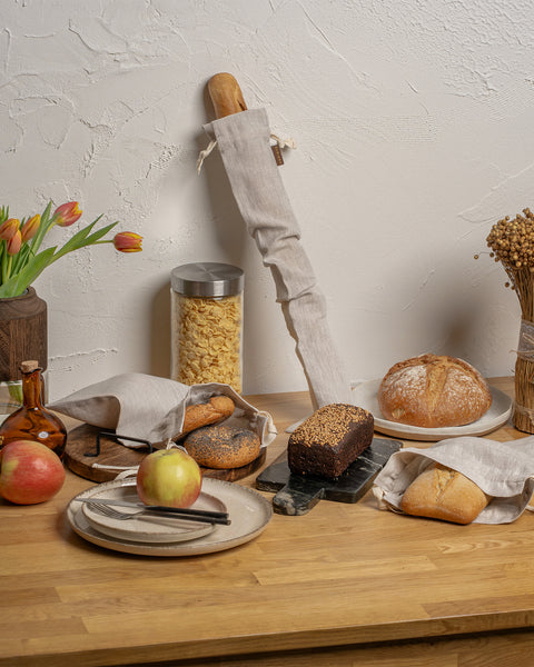 Wooden table with bread, apples, and flowers against a white wall.