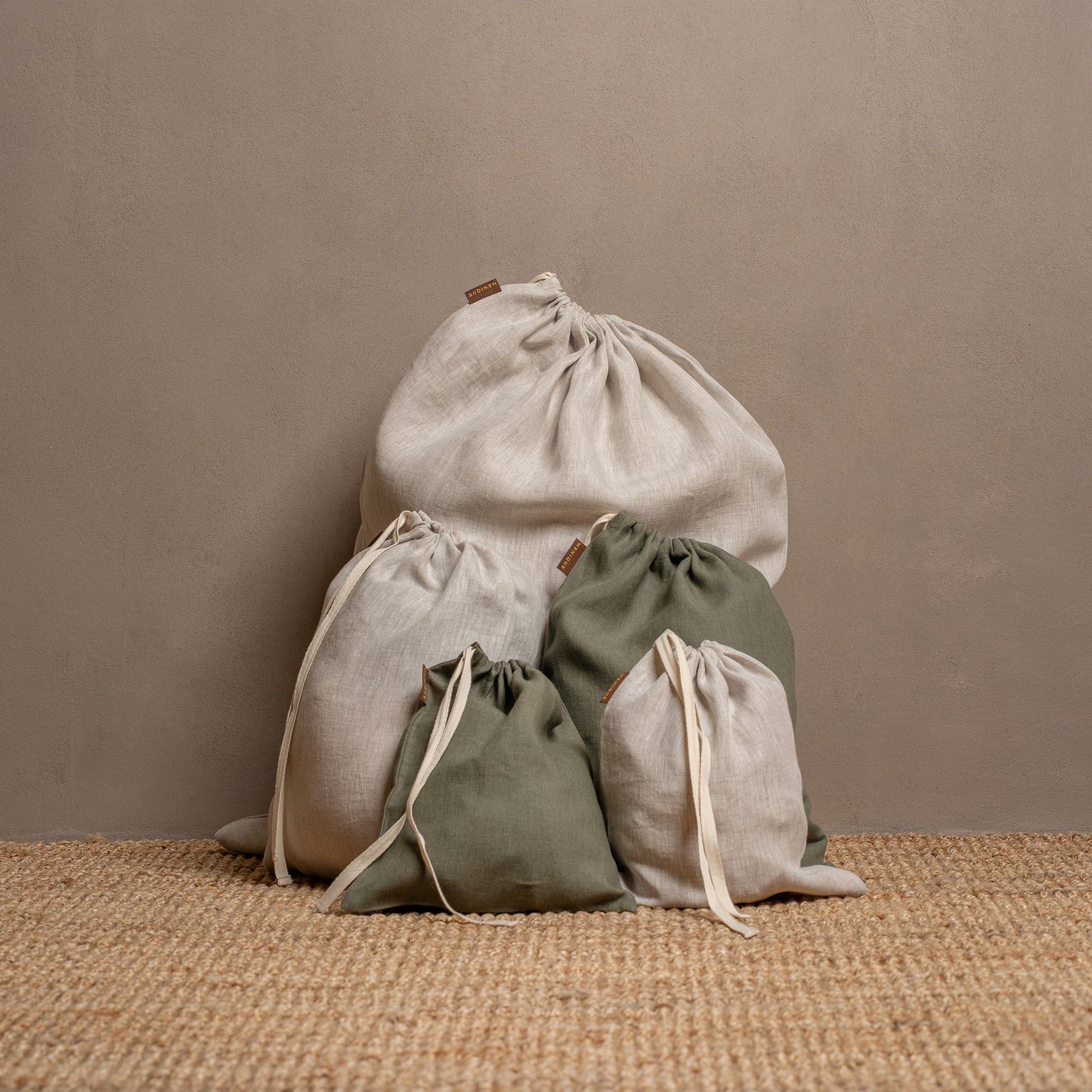 An open suitcase is neatly packed with four cloth drawstring bags of different sizes and colors (two olive green and two light beige) on a wooden surface.