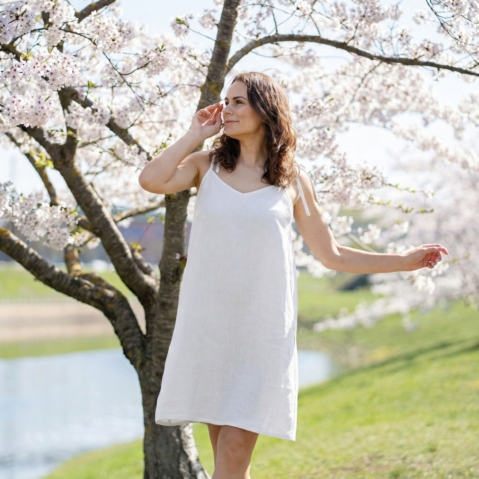 Woman wearing pure white linen summer dress with adjustable tie straps, breathable relaxed-fit dress styled outdoors under cherry blossom trees