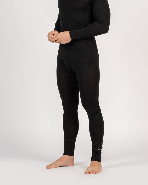 A slightly angled view of a person from the neck down standing barefoot against a white background, wearing a fitted, black long-sleeved thermal top and matching thermal leggings. Their hands are lightly clasped together in front of their waist.