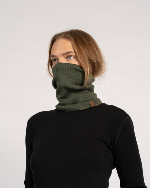 Woman wearing a dark green knitted Merino wool gaiter pulled up over the mouth and nose.