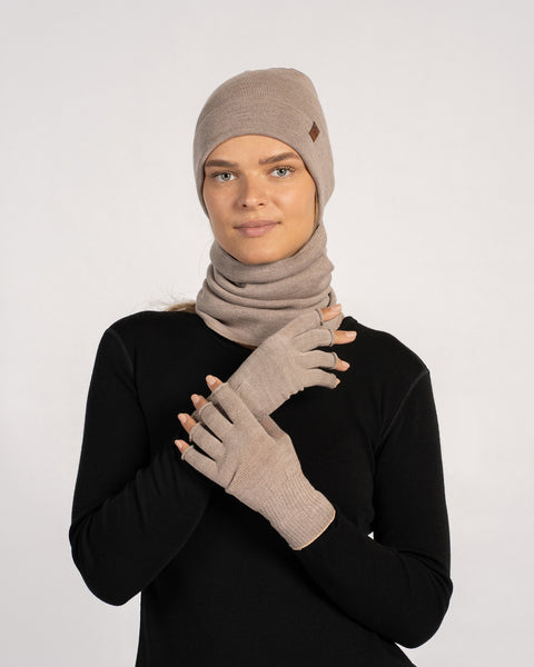 Woman wearing a creamy-beige beanie, matching gaiter and fingerless gloves, facing forward with hands crossed at chest.