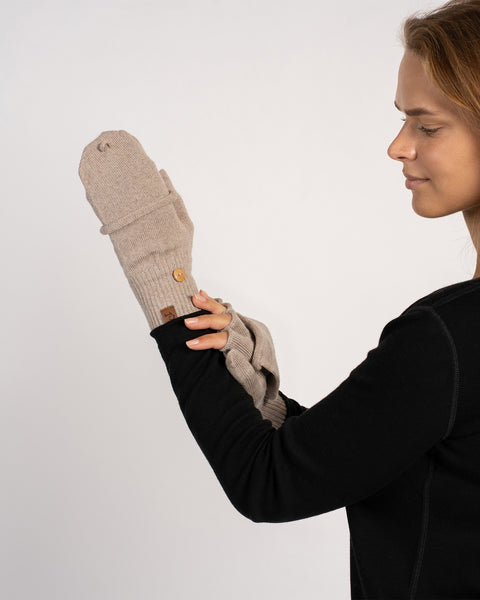 Close-up of a model’s hands showing a creamy-beige convertible mitten and a fingerless glove together (mitten flap visible).