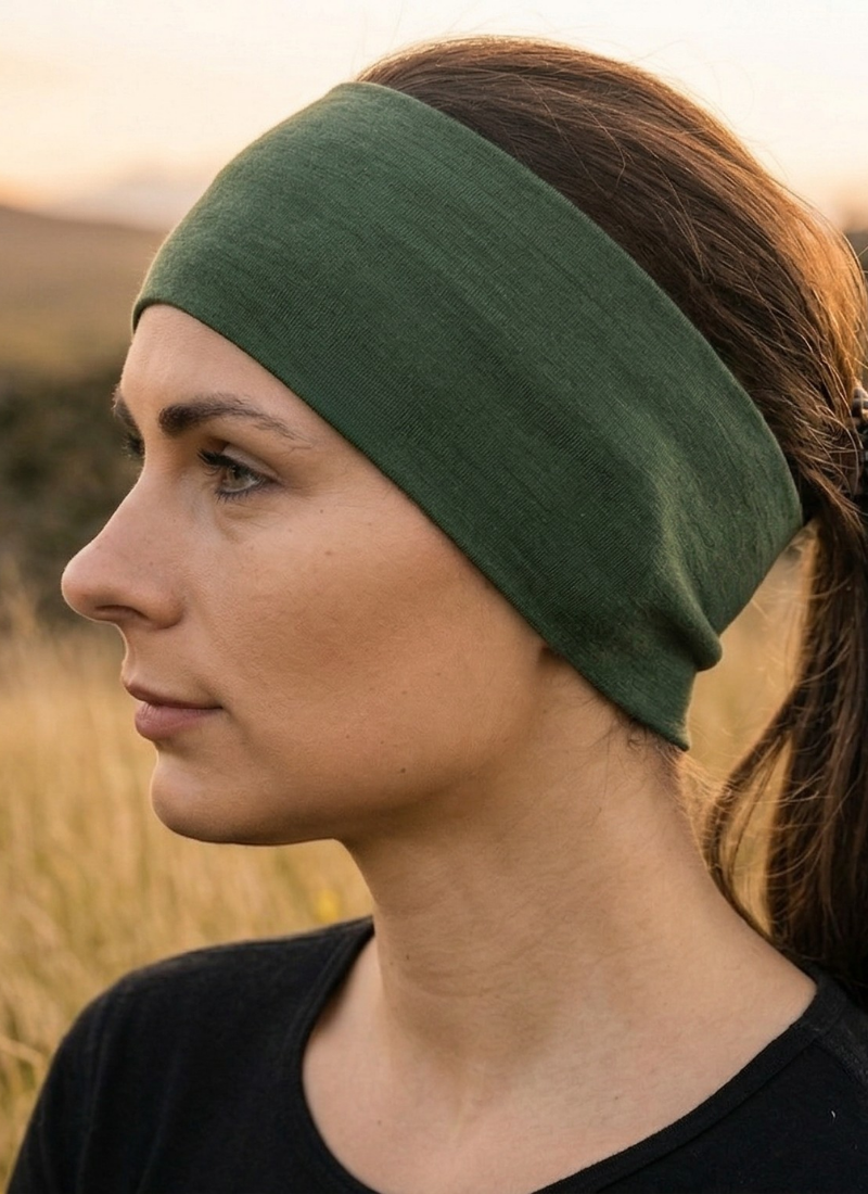 A close-up profile shot shows a woman outdoors wearing a wide, dark green fabric headband over her brown hair. She looks softly into the distance, dressed in a simple black top against a muted natural background.