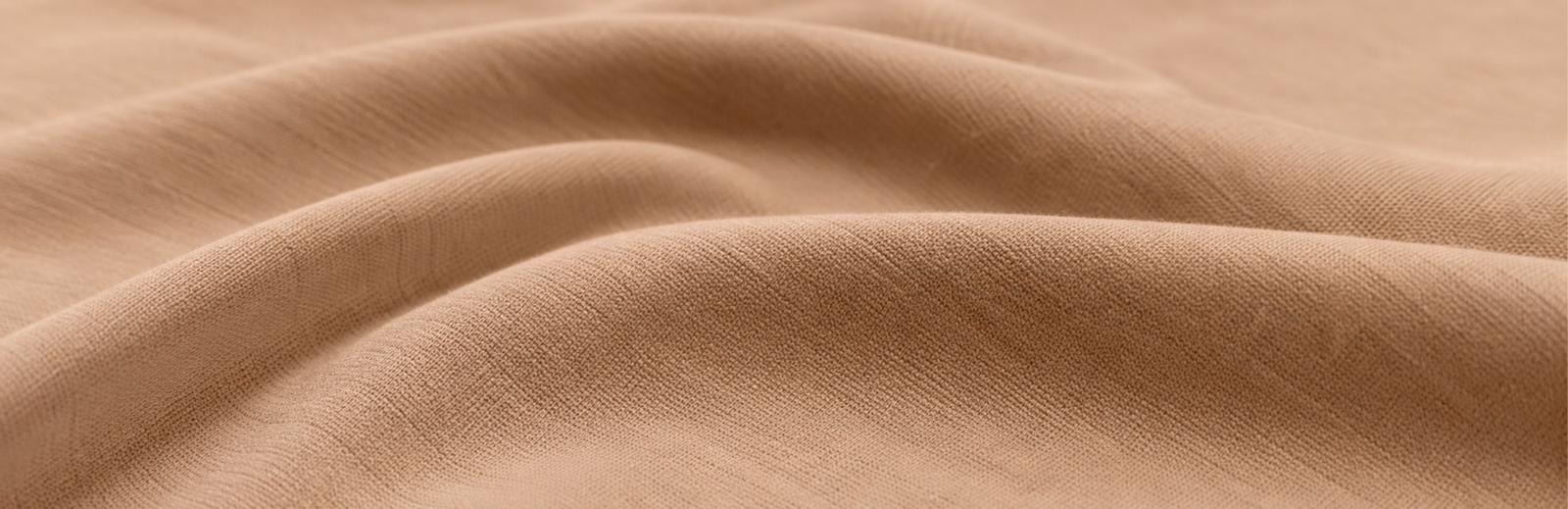 A close-up view of soft, light brown textured fabric draped to create gentle, rolling folds.