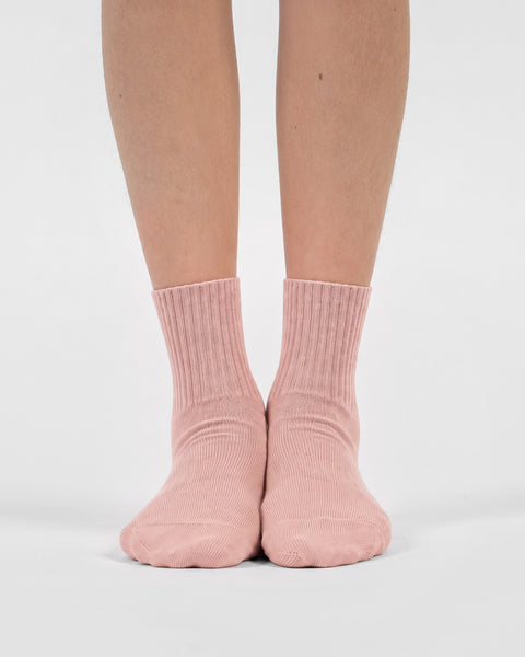 A front-facing view of a person's lower legs and feet standing side-by-side in light pink crew socks.
