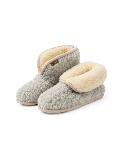 An angled view of a pair of light gray fuzzy ankle bootie slippers. The right slipper has its cuff folded down to reveal a plush cream-colored interior lining, and a "MENIQUE" tag is visible on the edge.