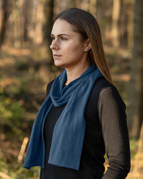Woman wearing a merino wool menique scarf and black long sleeve shirt standing in a forest